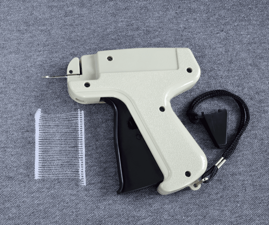Beige tagging gun lying on gray background with clear fasteners nearby.