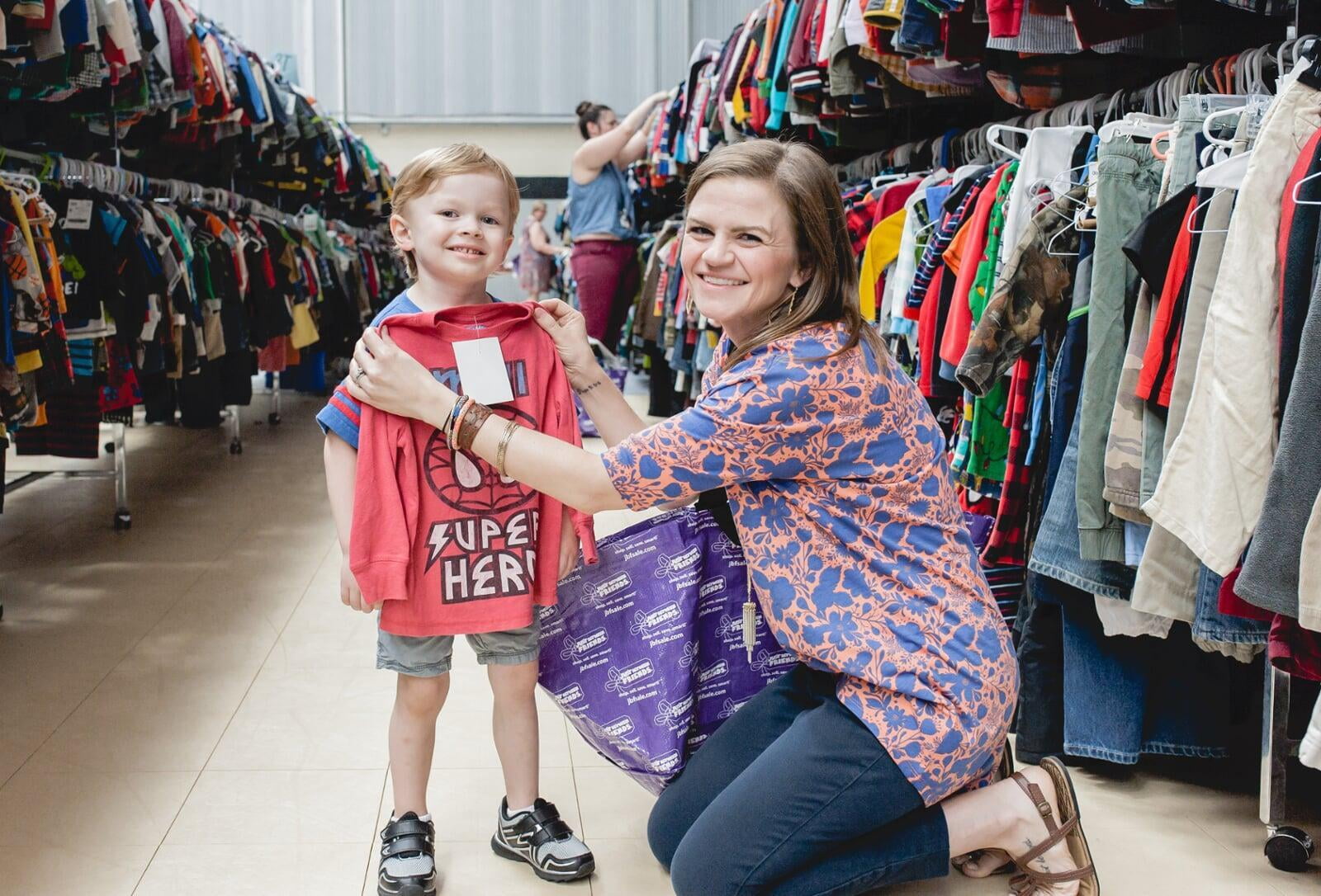 Mom holds up shirt to young boy to assess fit.