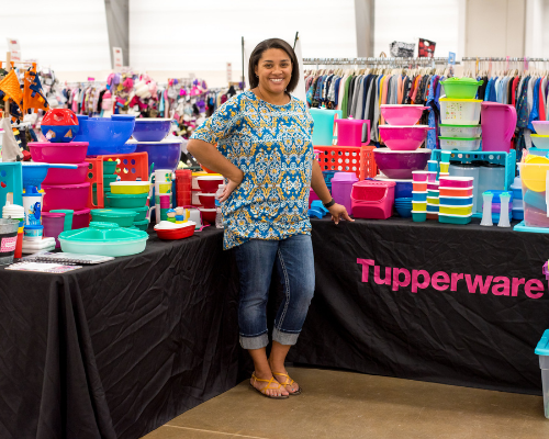 Female Tupperware vendor smiling standing in front of her booth at a JBF sale.