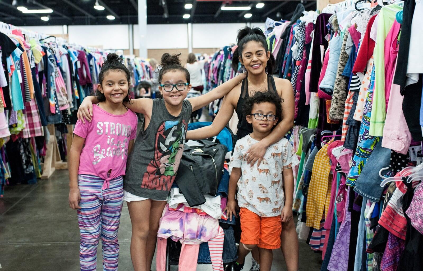 Mom and three kids smile in front of long aisle of clothing.