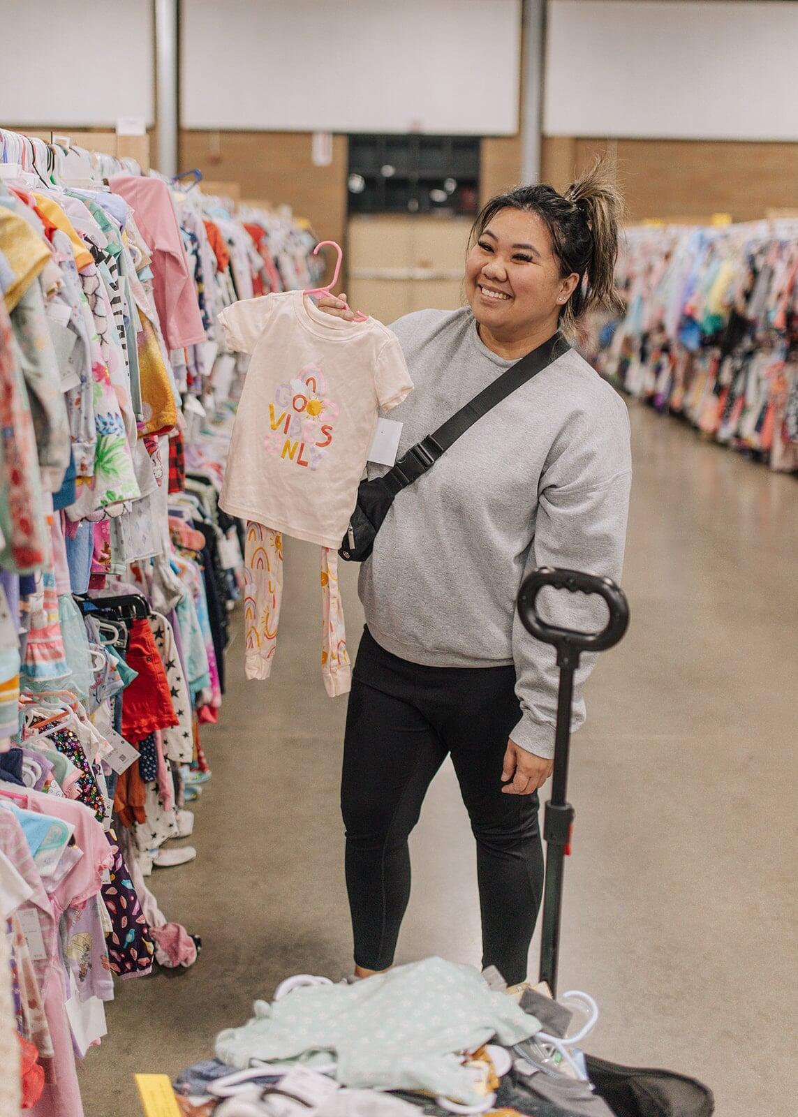 Smiling Mom holds up pajamas that she is purchasing as she shops long rows of girls clothing